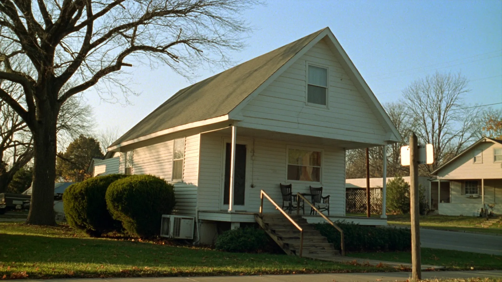 The front porch of a white clapboard house on a small town street, with a wooden ramp built over the front steps.